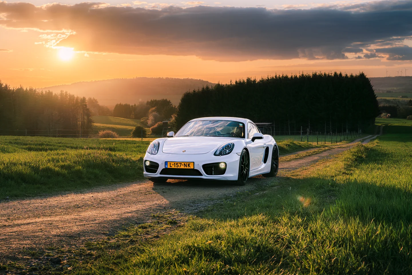 Witte Porsche op een landweg tijdens zonsondergang
